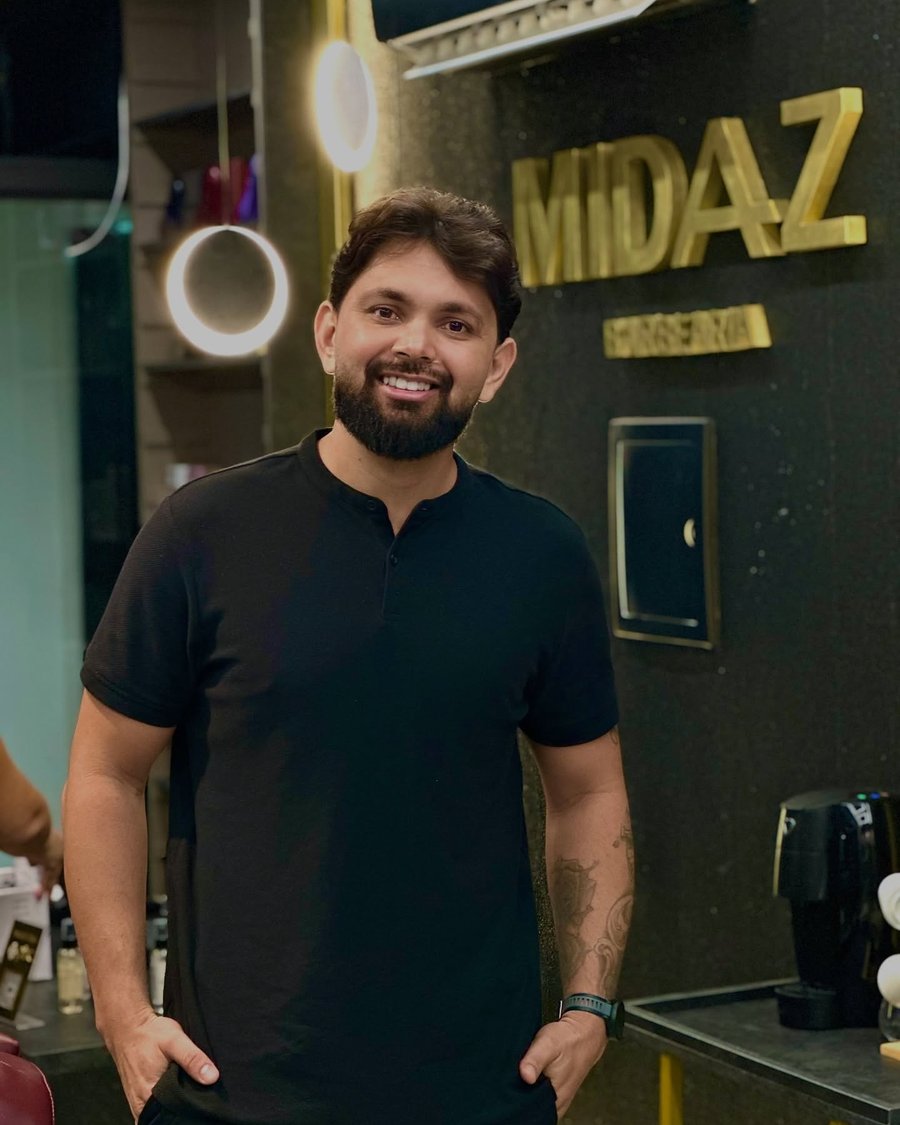 Barbeiro da Midaz sorrindo diante do letreiro dourado