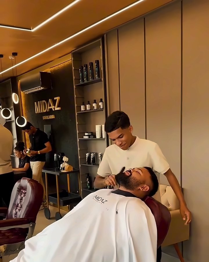 Barba sendo feita com o cliente reclinado, nome da Midaz ao fundo