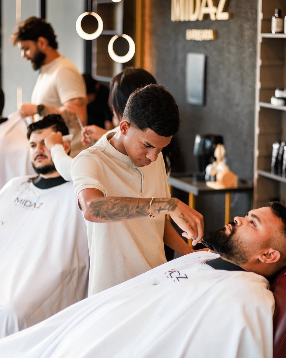 Salão da Midaz: barbeiro fazendo a barba de um cliente, com o nome dourado e os arcos de luz ao fundo