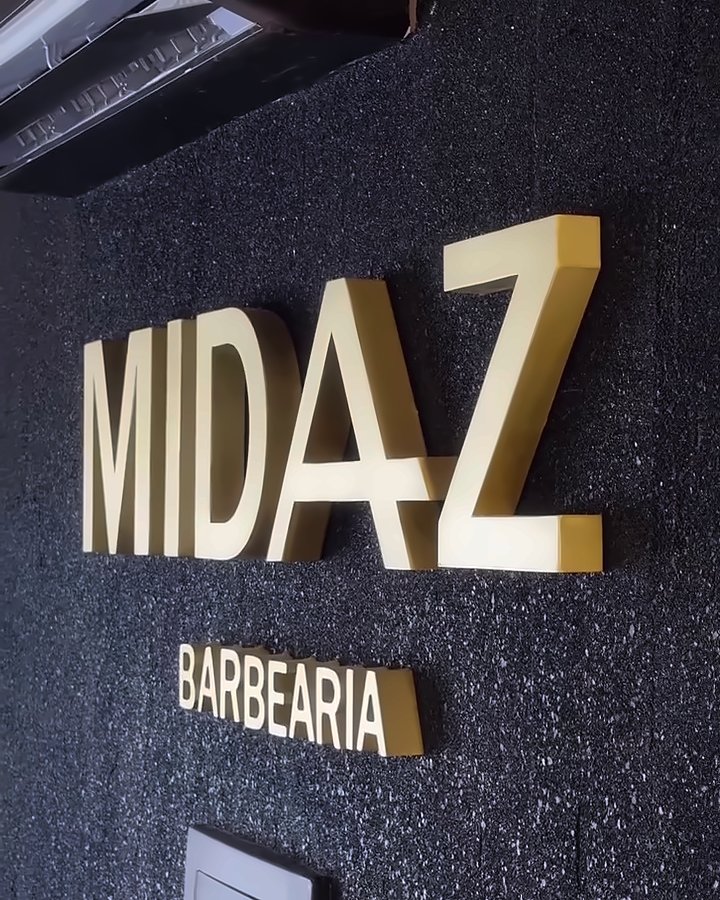 Letreiro MIDAZ Barbearia em letras douradas na parede escura
