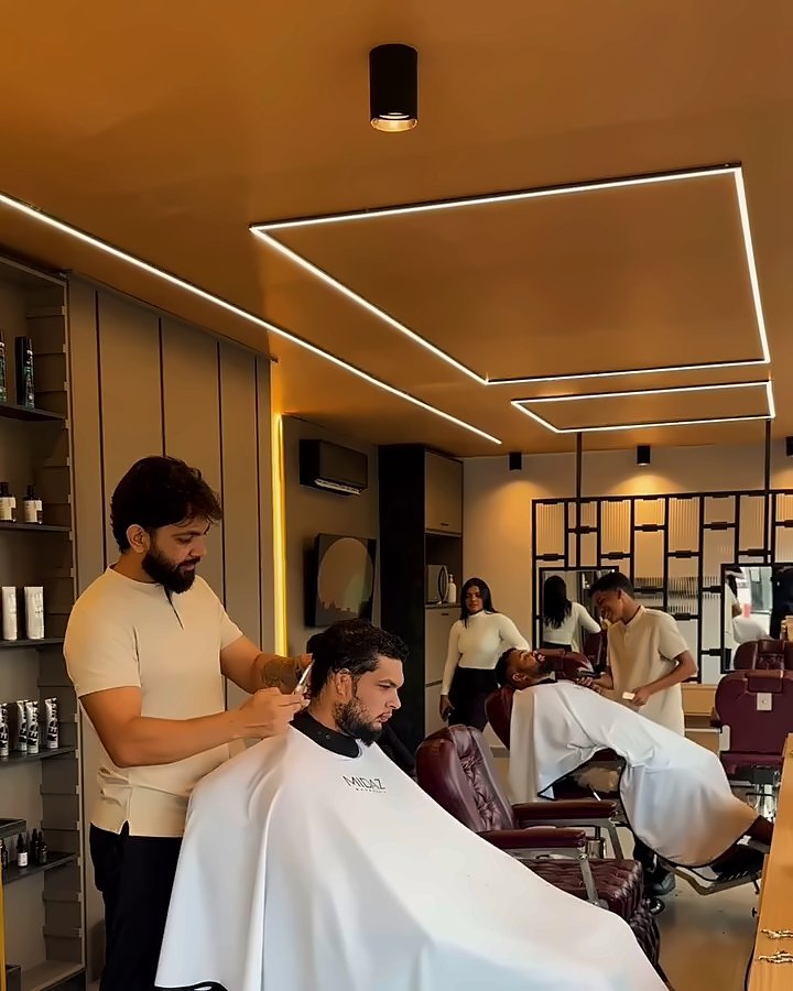 Salão da Midaz com teto de madeira, linhas de luz e barbeiros atendendo